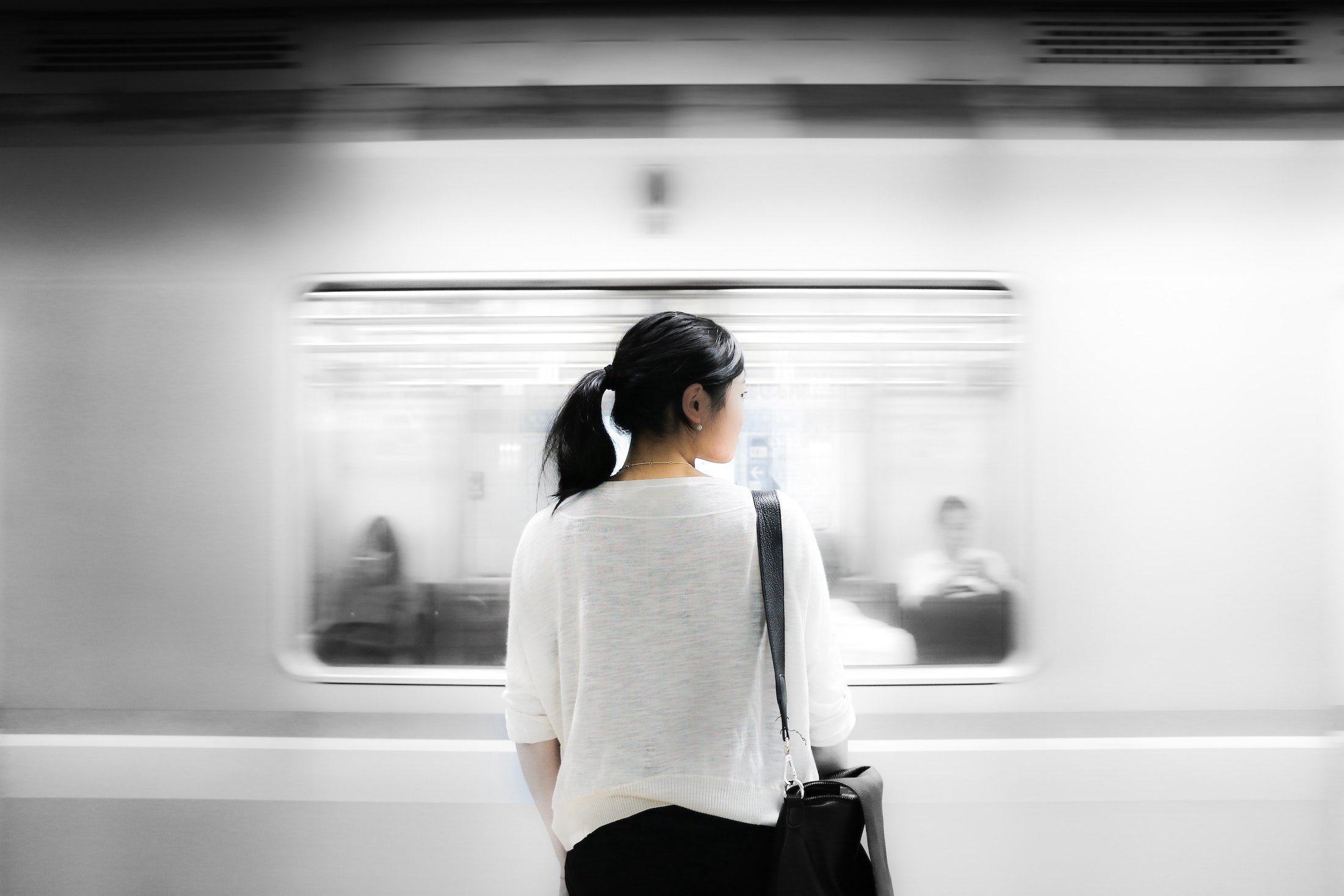 A young lady stands next to a passing subway train in her work attire