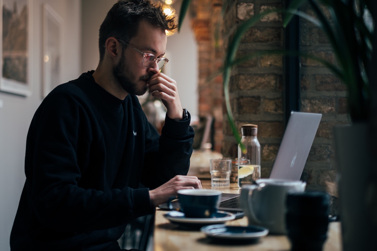 A man thinking deeply in front of his computer while enjoying coffee in a quiet environment