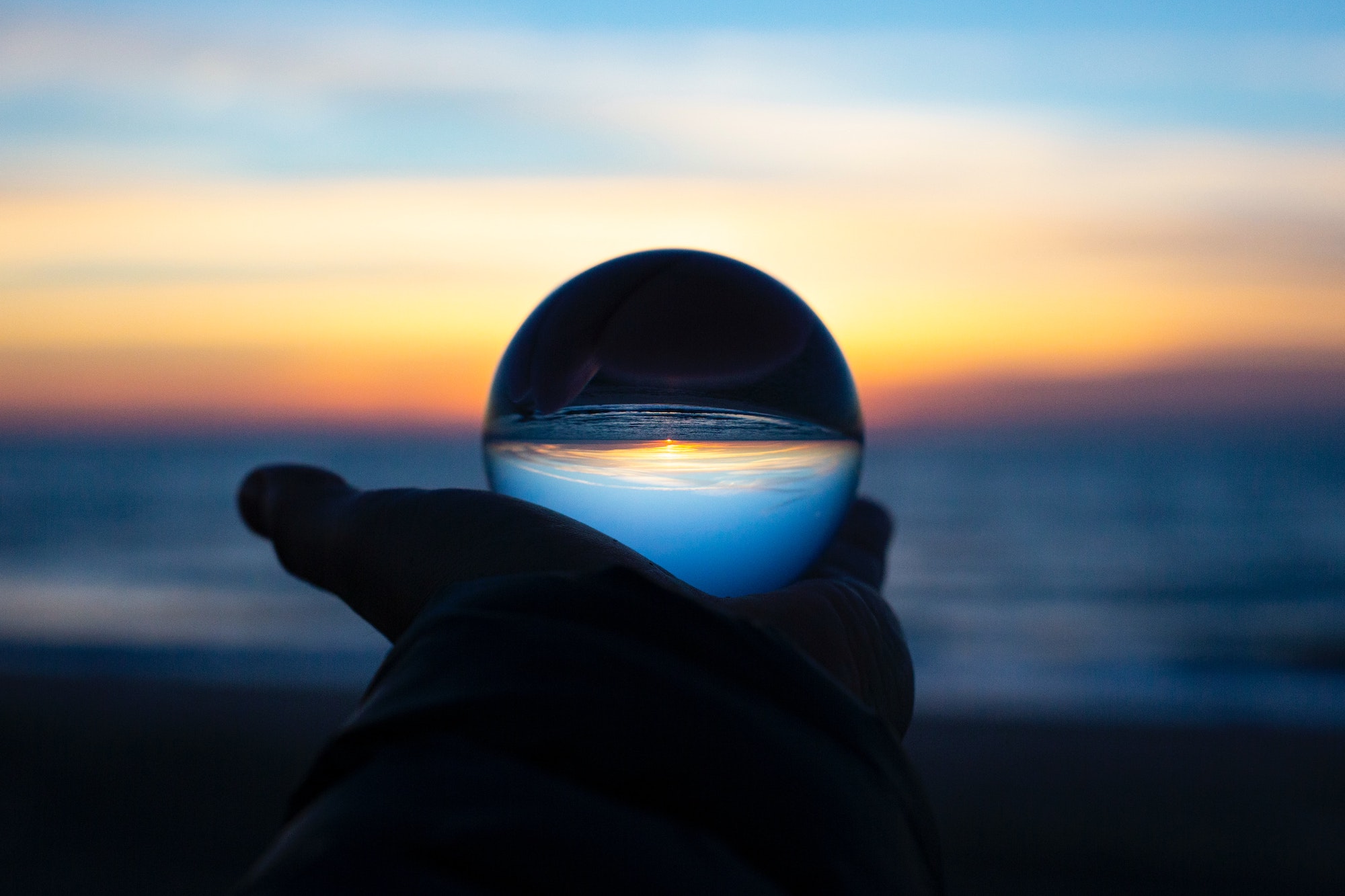 A hand holding a crystal ball with the sunset in the background